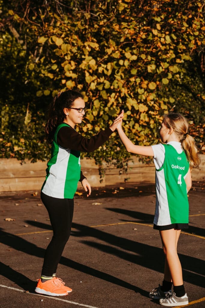 Two girls in matching green shirts are smiling together, captured in a lively outdoor scene.