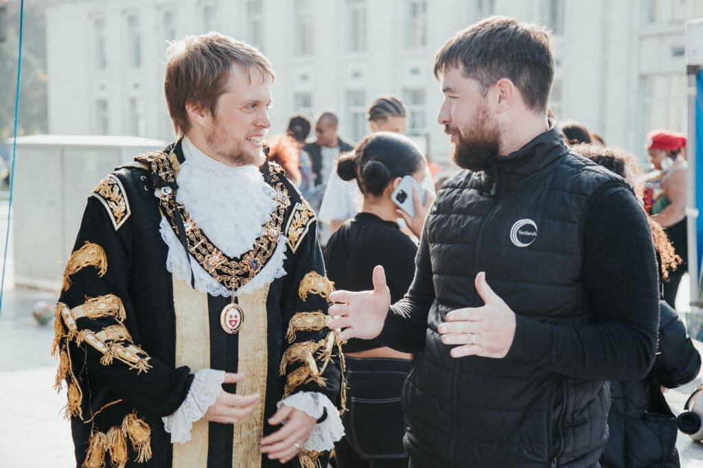 Two men wearing black and gold outfits conversing with one another.