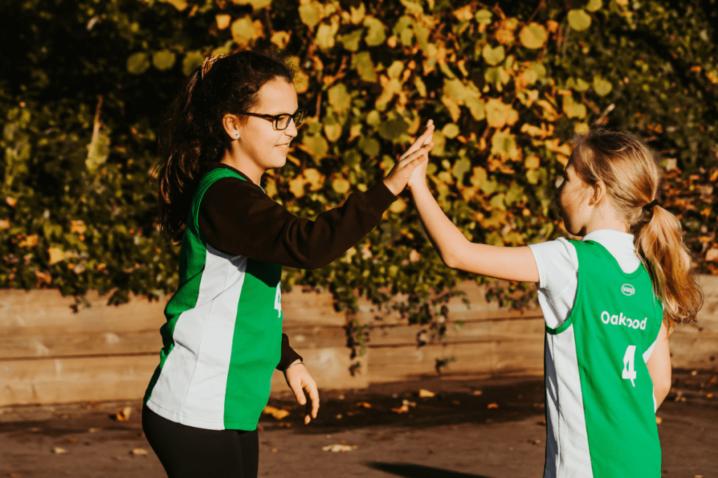 Two girls in green and white jerseys celebrate with a high five during a sports event.
