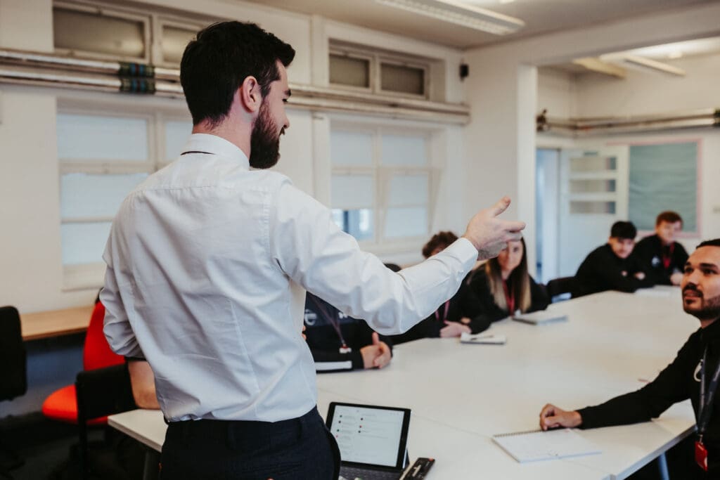 A man presenting to an audience, engaging with a group of attentive listeners in a conference setting.