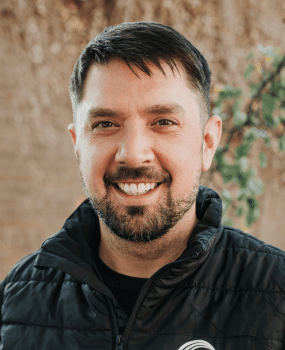 man with a beard wearing a black jacket stands confidently, showcasing a casual yet stylish appearance.